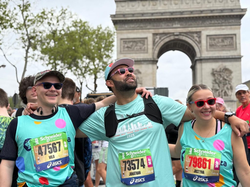 Milo, Johnnie and Justyna smiling before the start of the Paris marathon with the Arc de Triomphe behind them.